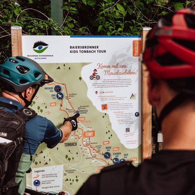 Biker stehen an einer Infotafel zur Kids Tonbach Tour und planen ihre Route