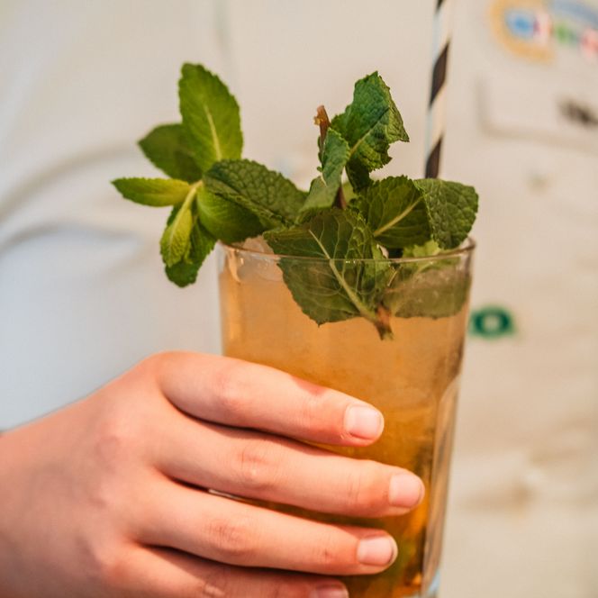 Ein Minikoch hält einen selbst gemixten Cocktail mit frischer Minze in der Hand.