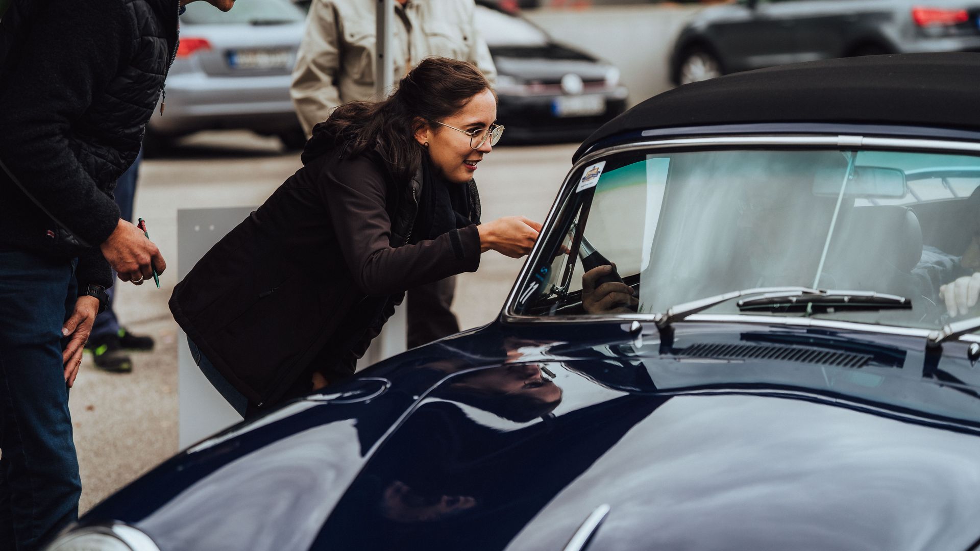 Eine Frau übergibt einem Teilnehmer der Baiersbronn Classic ein Begrüßungsgeschenk in seinen Oldtimer