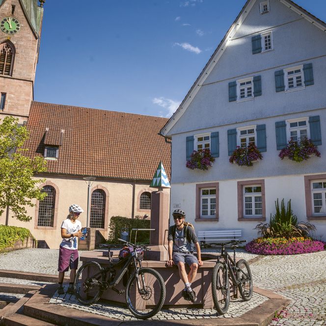 Biker machen Pause am Brunnen vor der Kirche in Baiersbronn
