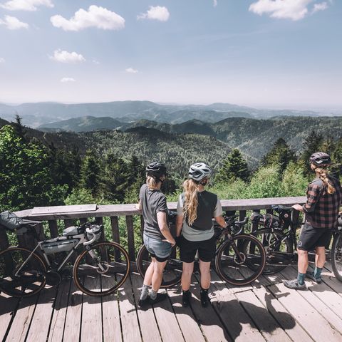 Personen stehen mit ihren Gravelbikes an einer Aussichtsplattform mit Blick auf die Landschaft im Schwarzwald