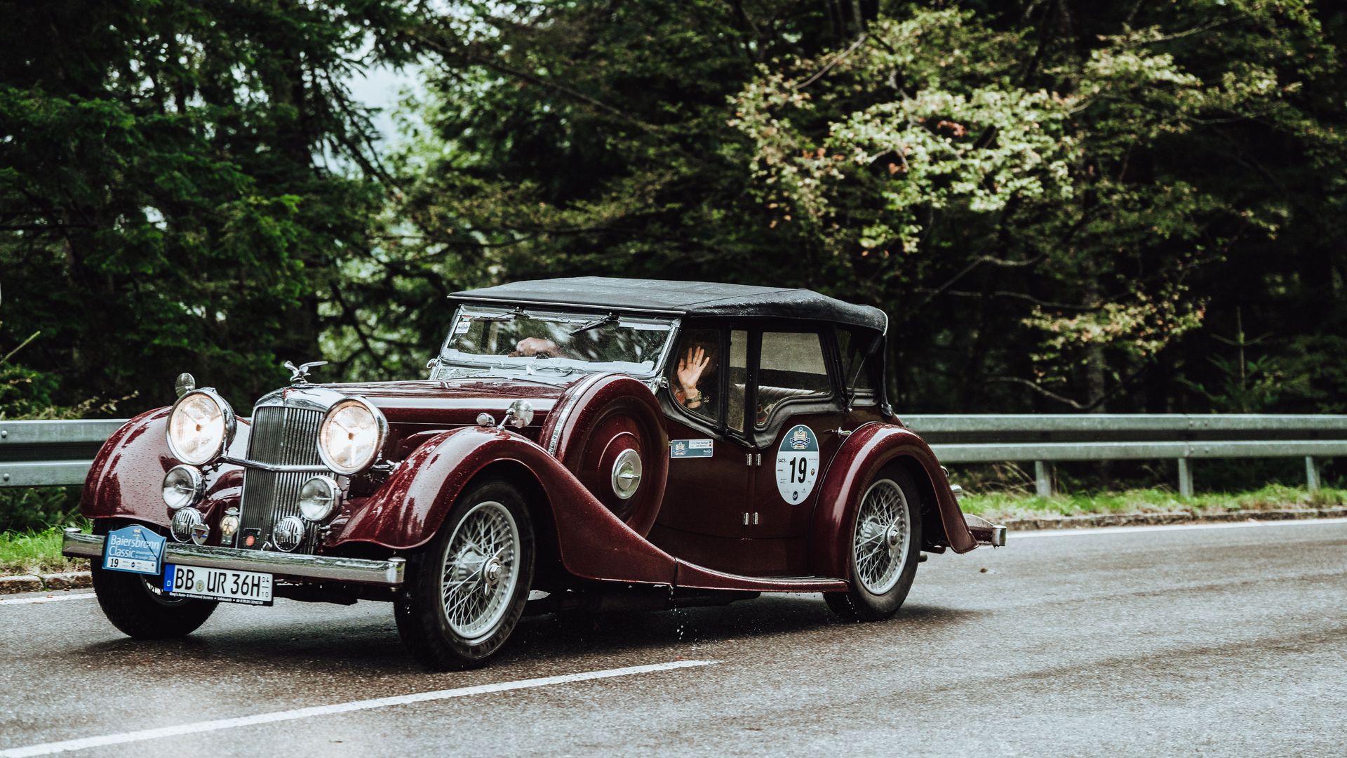 Ein Teilnehmer der Baiersbronn Classic winkt während der Fahrt aus seinem Oldtimer
