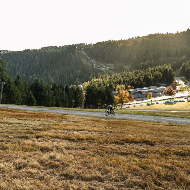 Ein Gravelbiker fährt auf einem Weg am Ruhestein mit Blick auf das Nationalparkzentrum im Hintergrund