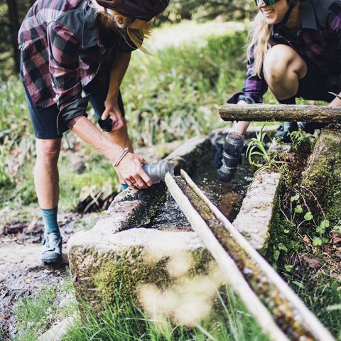 Biker füllen ihre Trinkflaschen an einem Wasserbrunnen im Wald auf