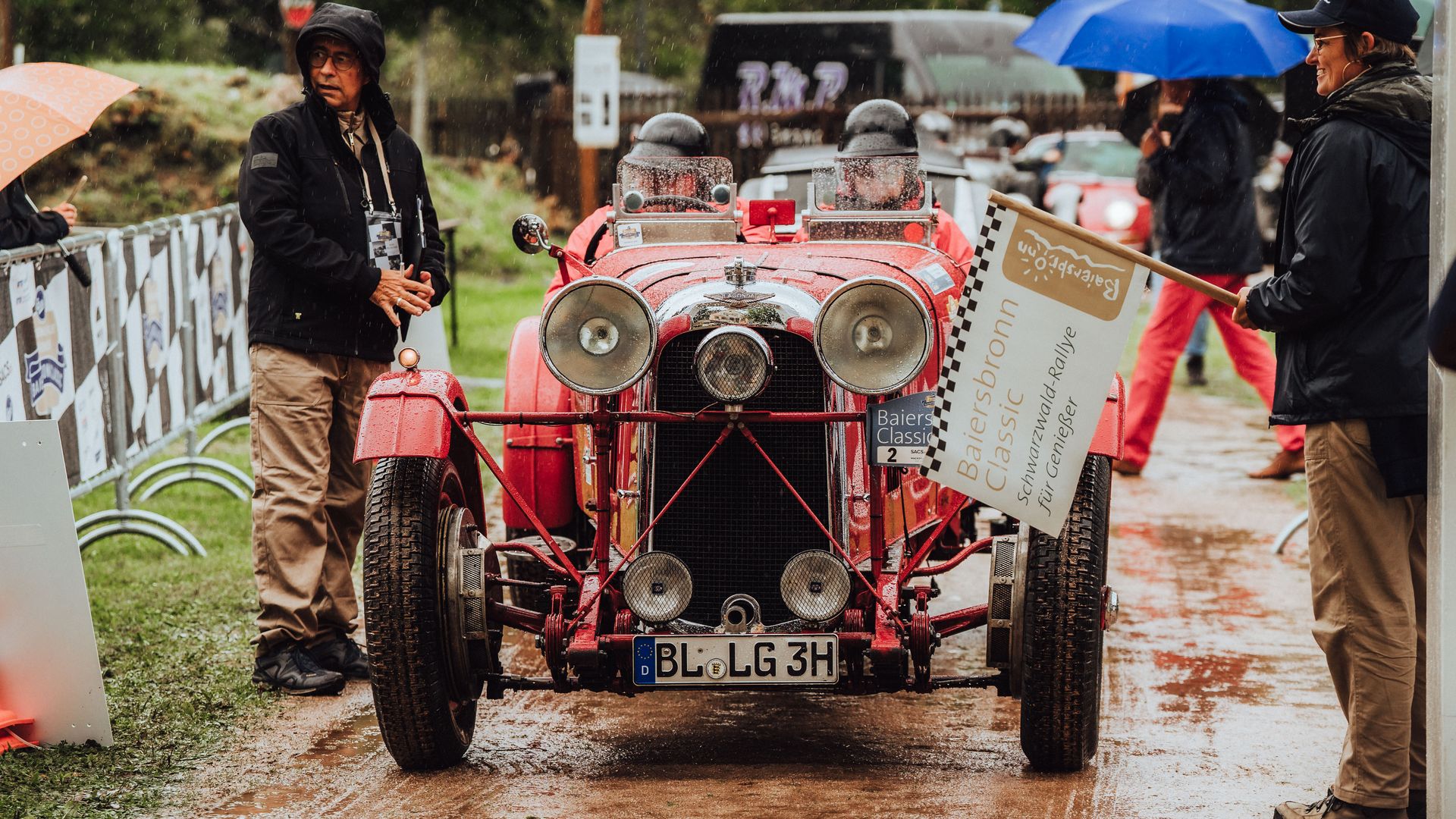 Teilnehmer der Baiersbronn Classic in einem roten Oldtimer-Cabrio bei der Startaufstellung im Regen
