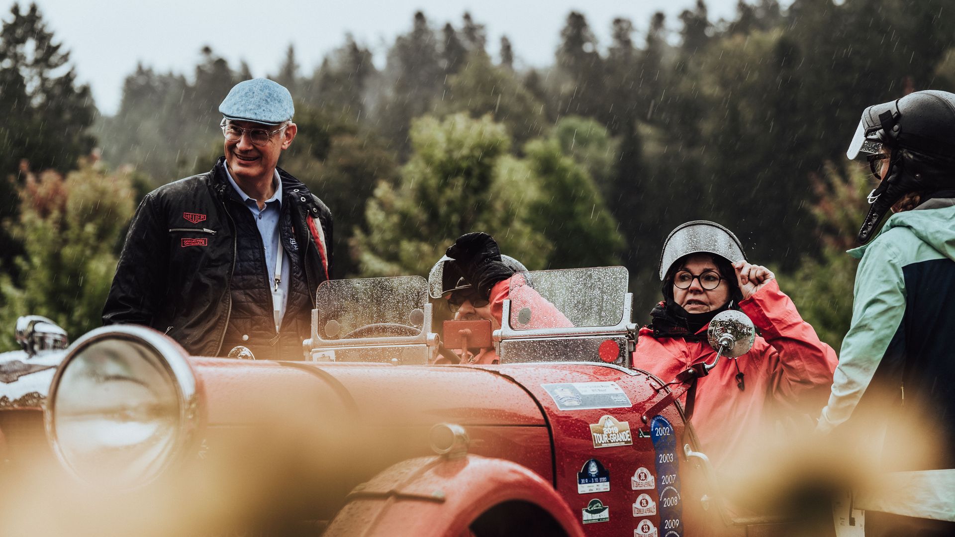 Teilnehmer der Baiersbronn Classic in einem roten Oldtimer-Cabrio bei der Startaufstellung im Regen