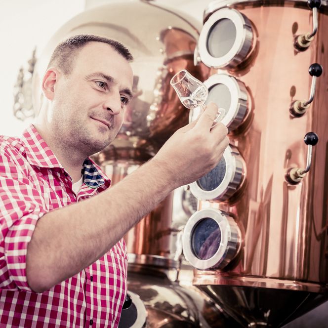 Ein Schnapsbrenner testet ein Glas Schnaps in seiner Brennerei