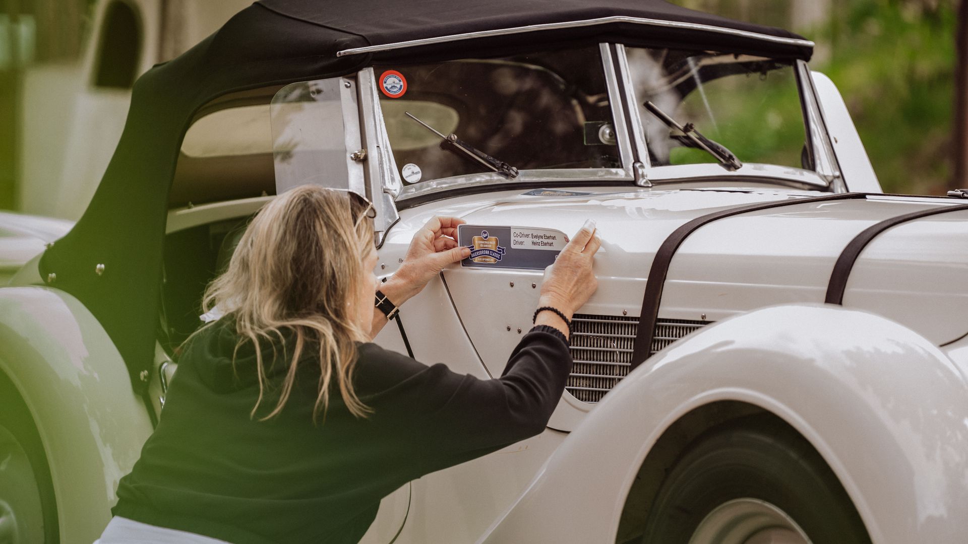 Eine Teilnehmerin der Baiersbronn Classic beklebt ihren Oldtimer mit ihrer Startnummer